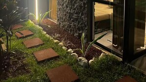A modern house with a stone facade, a glass door leading to a bedroom, and a garden with stepping stones. - Villa Refugio #2 (La Fortuna)