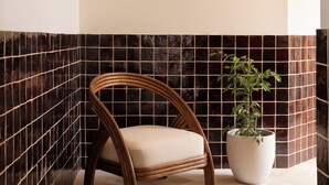A bathroom with a black and white tiled wall, a wooden chair, a potted plant, and a mirror with a geometric frame.