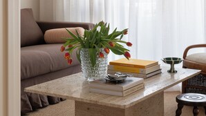 A living room with a sofa, a coffee table with books and a vase of tulips, a chandelier, and sheer curtains.