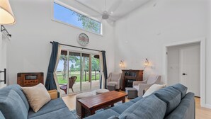 A spacious living room with a large grey sofa, a wooden coffee table, and a TV. There is a sliding glass door leading to a patio with outdoor furniture. - New Waterfront Luxury Cabin on Lake Winnipeg (Matlock)
