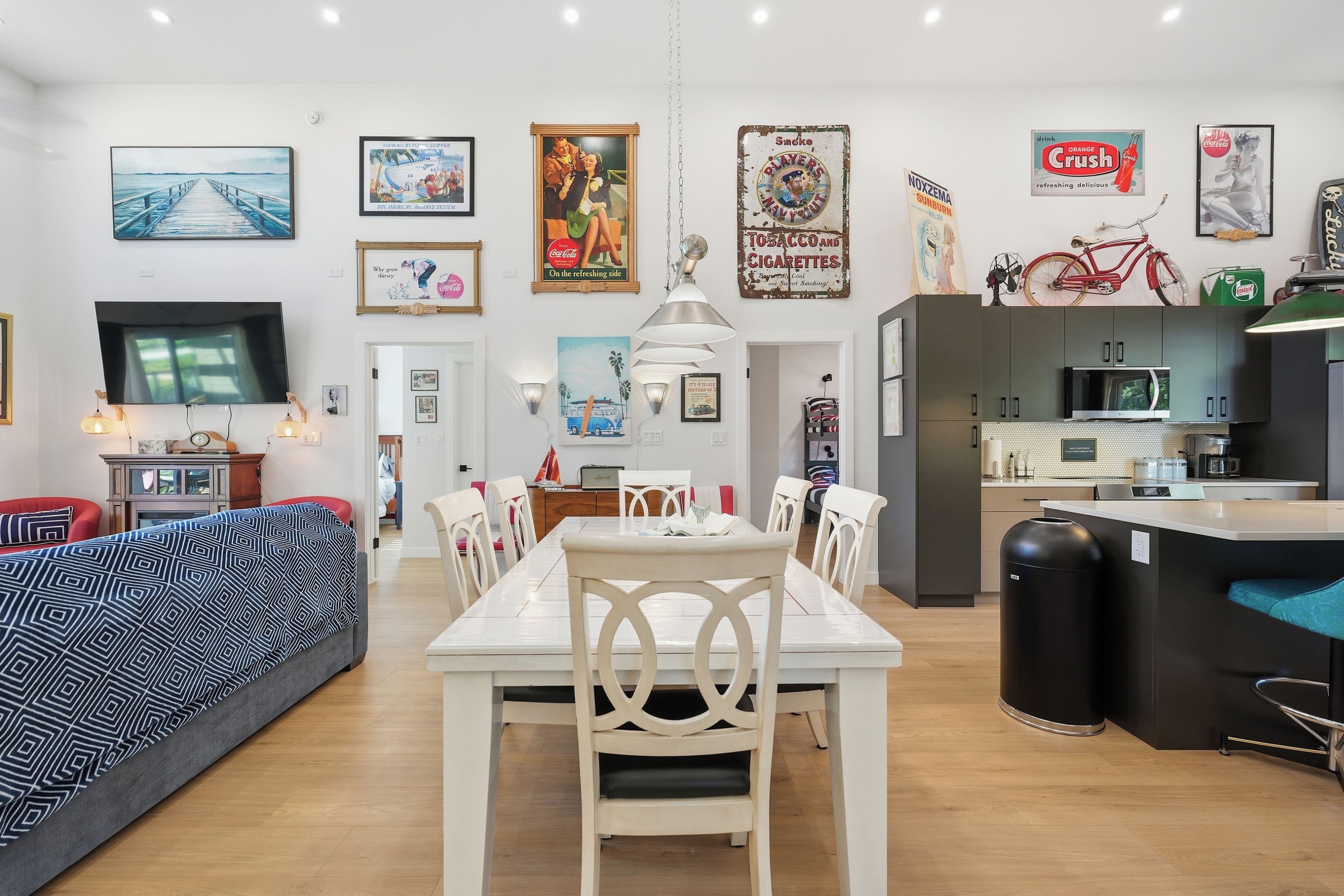 A modern living room with a sofa, dining table, and chairs, a kitchen area with a microwave, and various framed pictures on the walls.