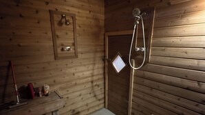 A wooden cabin with a bench, a small table, and a shower area.