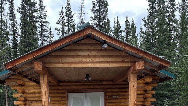 A log cabin with a porch, two Adirondack chairs, and a door.