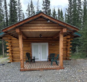 Una cabaña de madera con un porche, dos sillas Adirondack y una puerta.