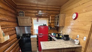 A compact kitchen with wooden walls, a red refrigerator, a stove, and a sink. There are two stools and a countertop.