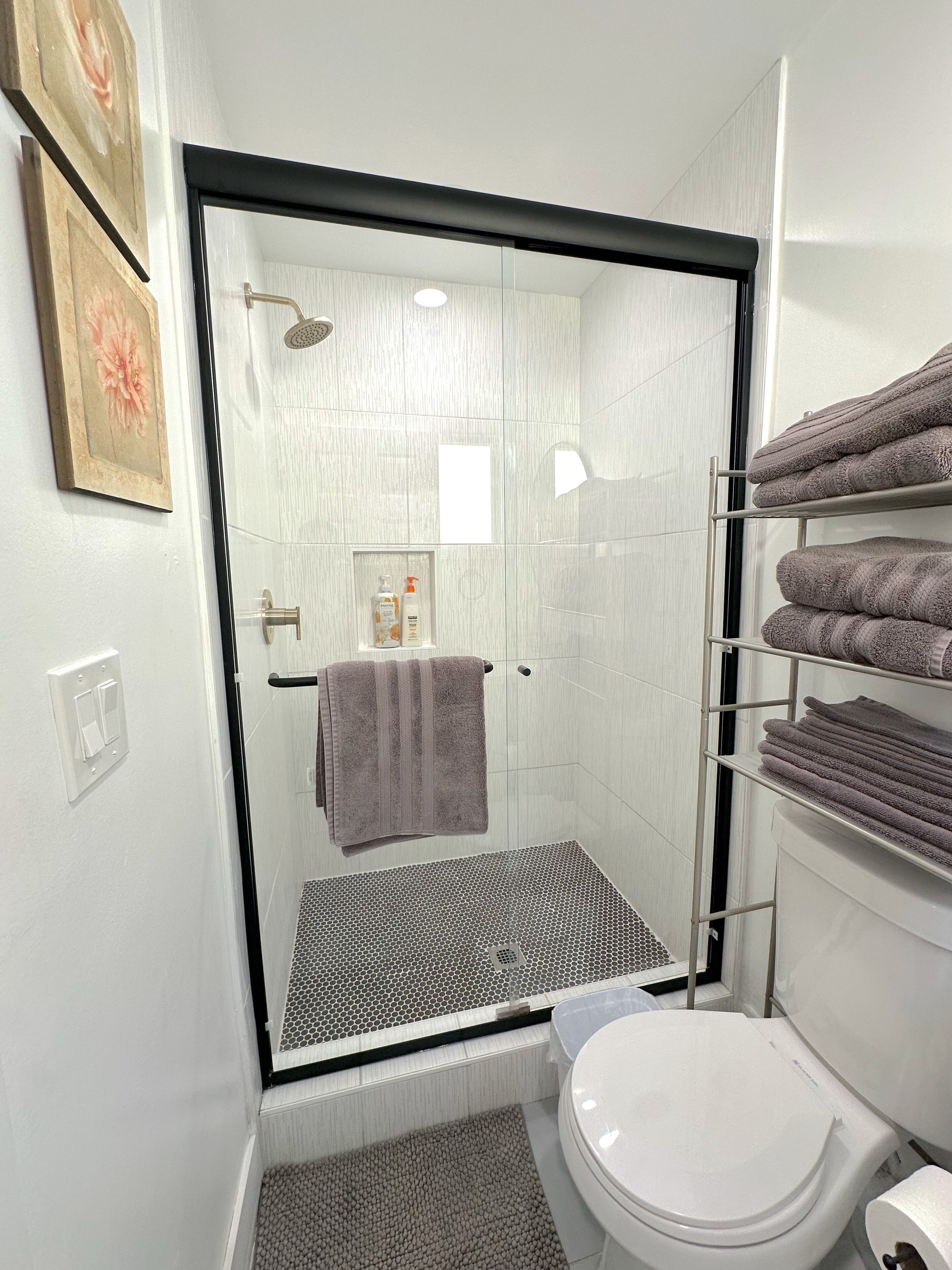 A modern bathroom with a glass-enclosed shower, a toilet, and a towel rack with folded towels.