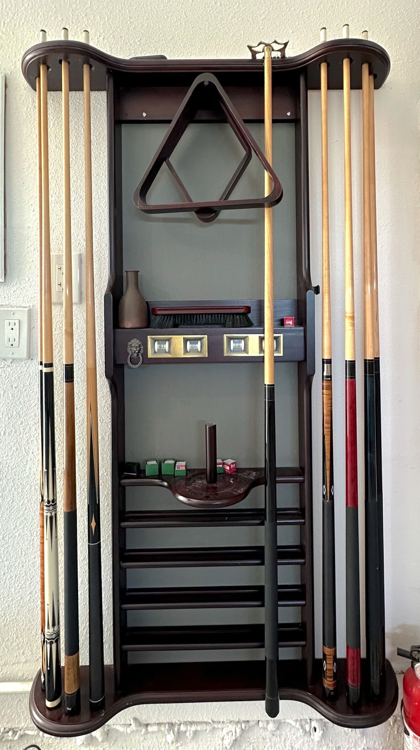 A billiards rack with various cue sticks and a brush.