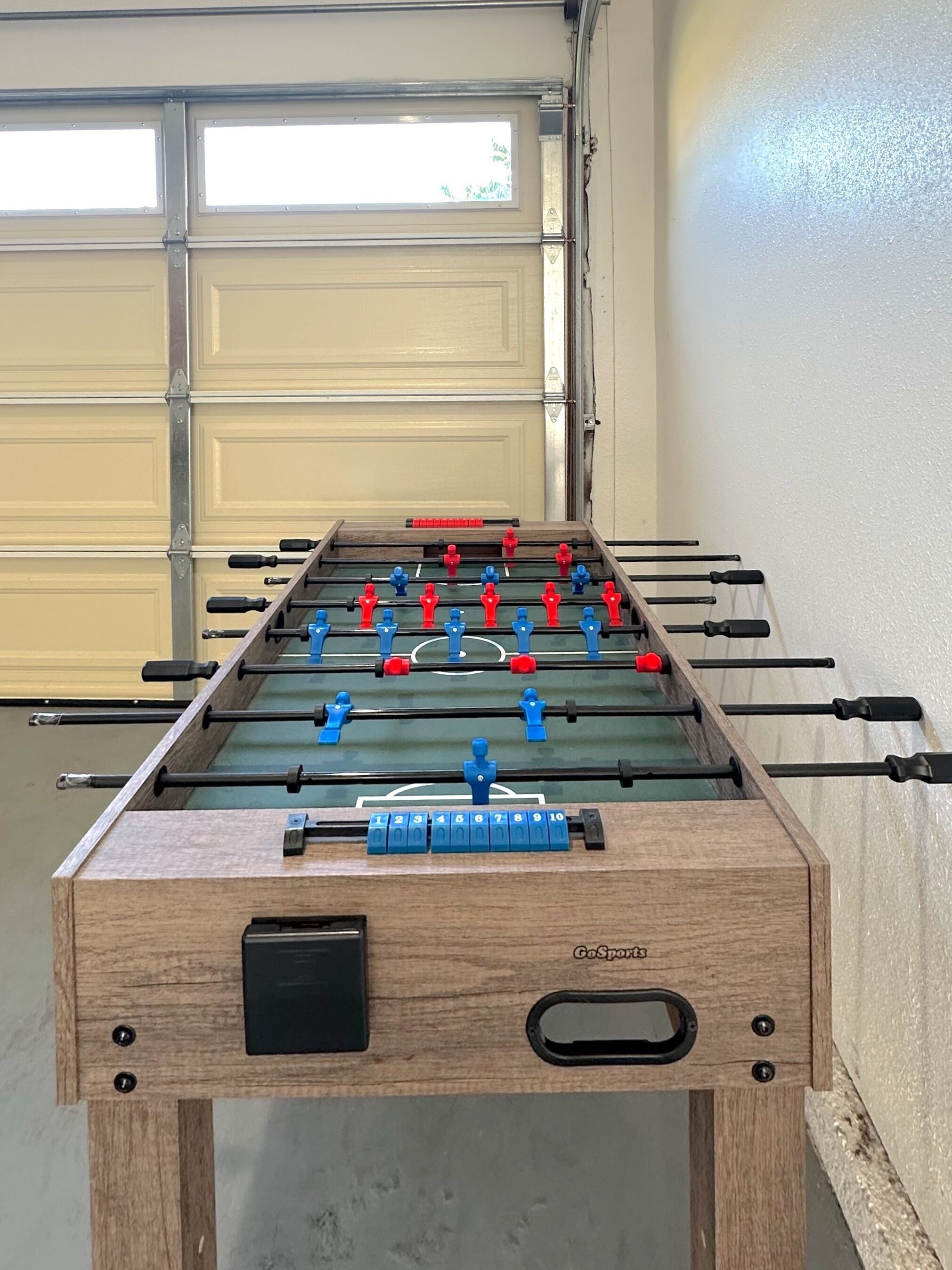A foosball table in a garage with a garage door in the background.