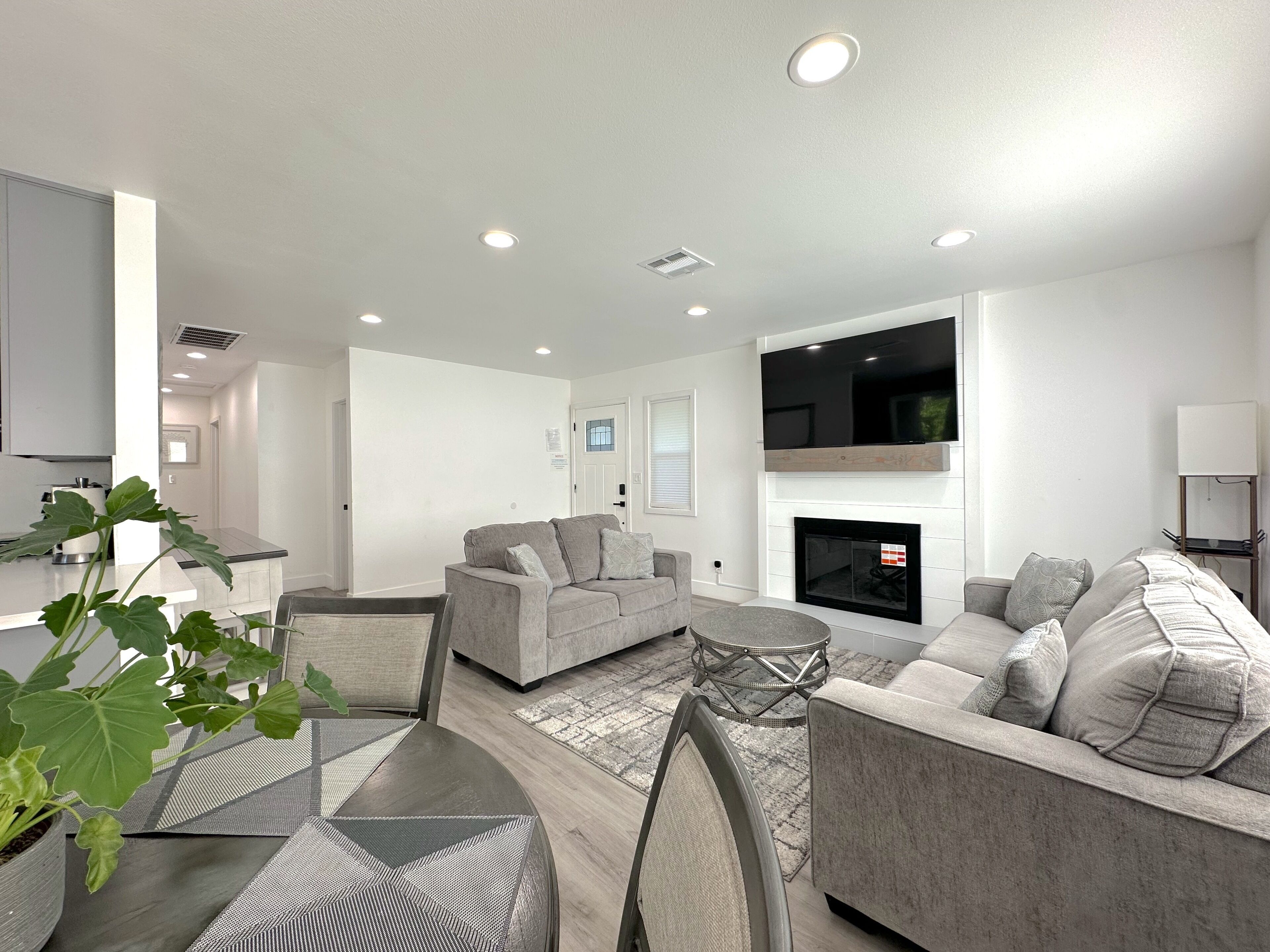 A modern living room with a fireplace, two sofas, a coffee table, and a dining area with a chair and a plant.