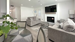 Una sala moderna con chimenea, dos sofás, una mesa de centro y un comedor con una silla y una planta.