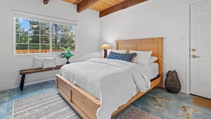 A bedroom with a wooden bed, a bench, a window with a view, and a ceiling fan.