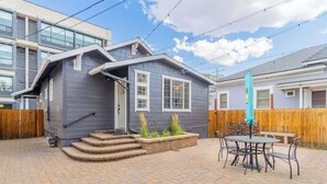 A two-story house with a grey exterior, a front porch with steps, and a patio area with a table and chairs. - Stylish 2-bedroom Walking Distance to Downtown (Reno)