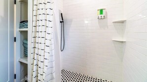 A bathroom with white tiled walls, a shower with a black rainhead, a white and black checkered floor, and a green soap dispenser. - Stylish 2-bedroom Walking Distance to Downtown (Reno)
