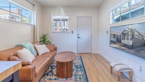Ein modernes Wohnzimmer mit Ledersofa, rundem Holztisch und einem großen Fenster mit Blick auf ein Haus.