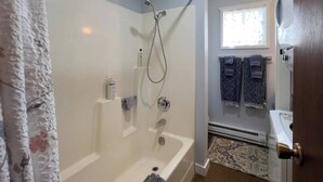 Baño con bañera, ducha y ventana con toallas colgadas.
