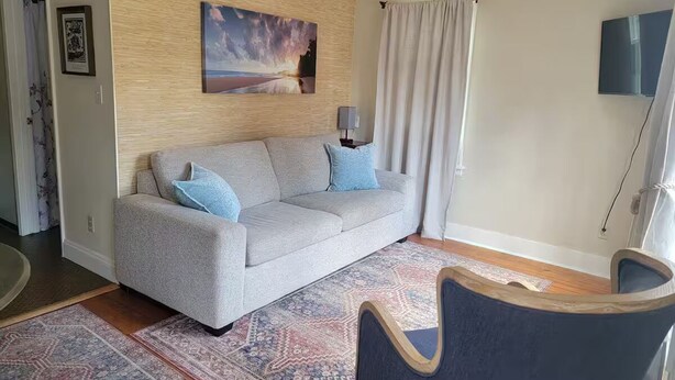 Una sala de estar con un sofá gris, cojines azules, un tapete estampado y un cuadro en la pared.