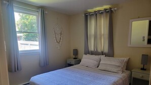 Un dormitorio ordenado con cama, dos mesitas de noche, un tocador, un espejo montado en la pared y una decoración de atrapasueños.
