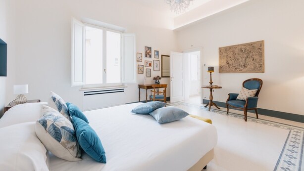 A bedroom with a large bed, a chandelier, a desk, and a chair. - Premium Apartment - Helichrysum (Montepulciano)