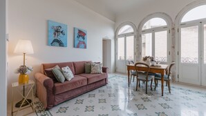 A living room with a sofa, a dining table with chairs, a lamp, and two paintings on the wall. - Premium Apartment - Helichrysum (Montepulciano)
