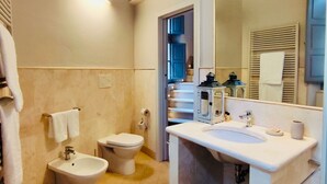 A bathroom with a bidet, toilet, sink, and a large mirror. There is a towel rack and a basket with towels. - Quadruple Room - Dill (Montepulciano)