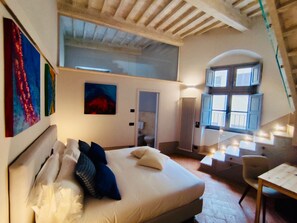 Quarto com cama, janela com persianas, radiador e obras de arte na parede.