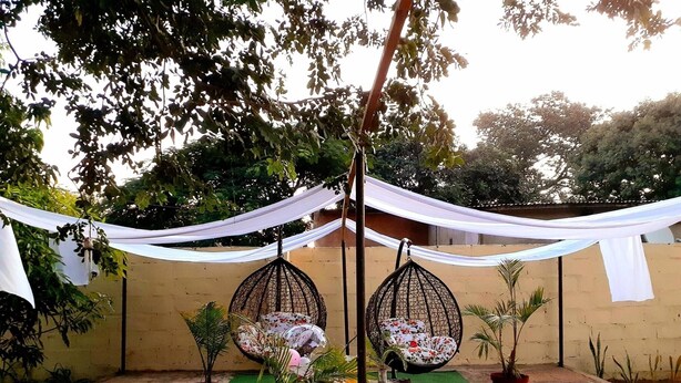 A patio area with two hanging chairs, a small table, and potted plants. - Chobe Oasis Guest House (Kasane)