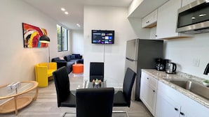 A modern kitchen with white cabinets, a stainless steel refrigerator, and a built-in microwave. There is a dining area with a glass table and black chairs. - Metro Park Hotel (Miami)