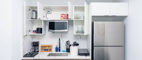 Una cocina moderna con muebles blancos, microondas integrado, refrigerador de acero inoxidable y cafetera.