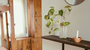 Una habitación con literas, un armario de madera, una repisa con una planta y una vela, y un espejo.