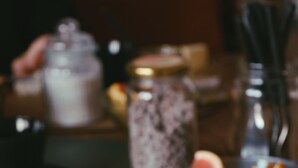 Una mesa con una taza y platillo negros, un frasco de vidrio y un cuenco de fruta.