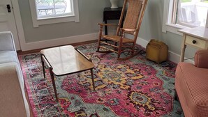 Une pièce avec un plancher en bois, un tapis à motifs, un fauteuil à bascule, une petite table et une lampe.