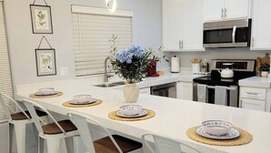 A modern kitchen with white cabinetry, a central island with bar stools, and pendant lighting. - The Bluebonnet Peak (Brownsville)