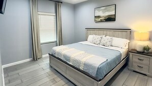A bedroom with a bed, a ceiling fan, a nightstand, a lamp, and a window with curtains. - The Bluebonnet Peak (Brownsville)