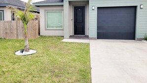 A residential house with a garage, a front door, and a small lawn with a palm tree. - The Bluebonnet Peak (Brownsville)
