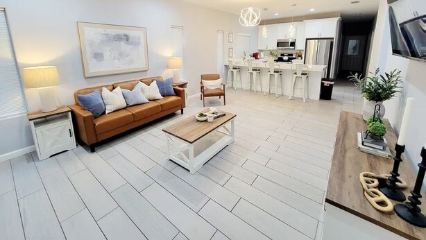 A modern living room with a brown leather sofa, a glass coffee table, and a ceiling fan. - The Bluebonnet Peak (Brownsville)