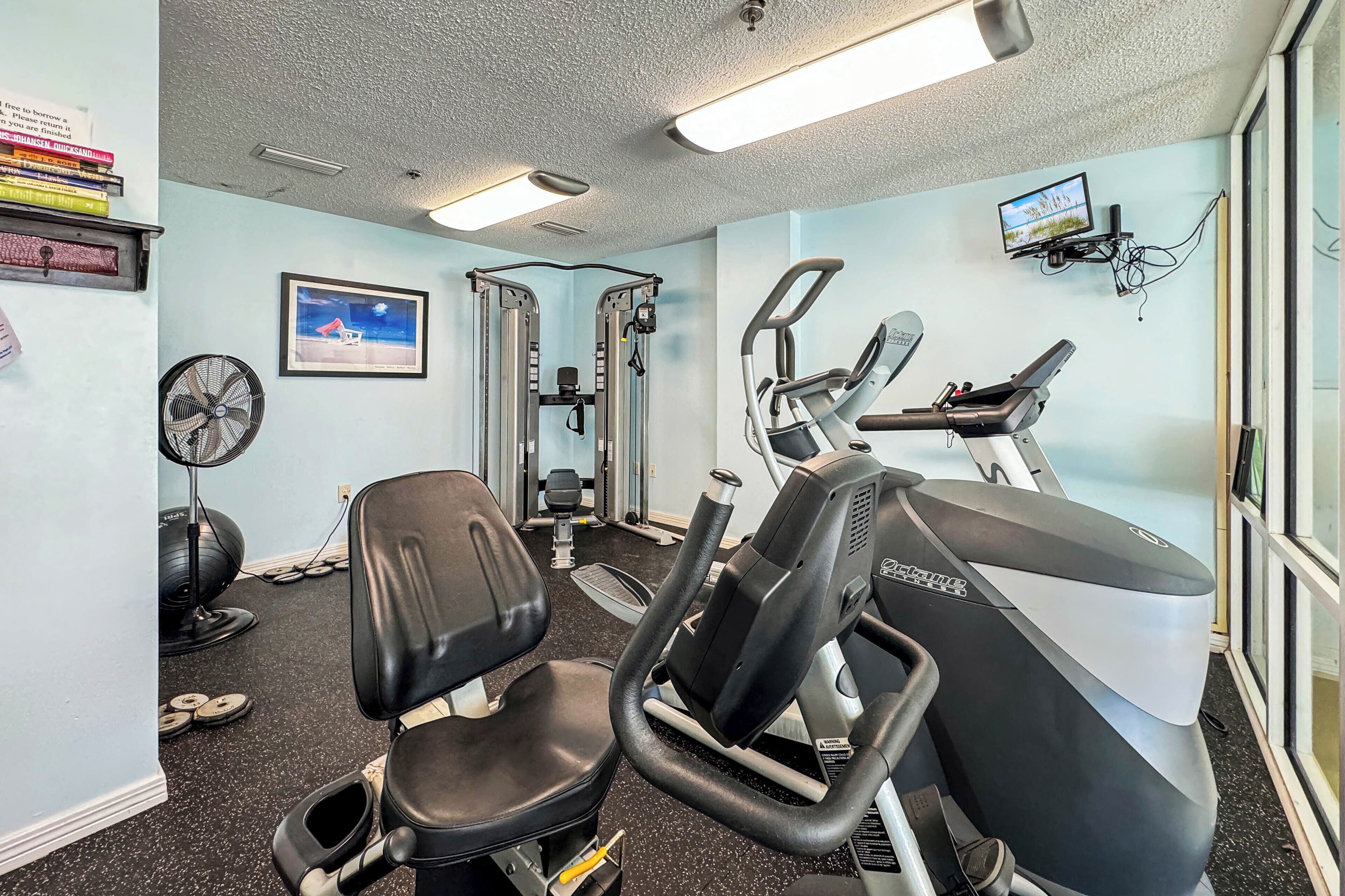 A gym with exercise equipment, a fan, and a TV on the wall.