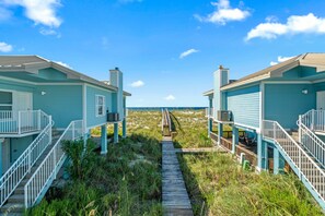 A pathway leading to two light blue beach houses with white railings and a view of the beach.