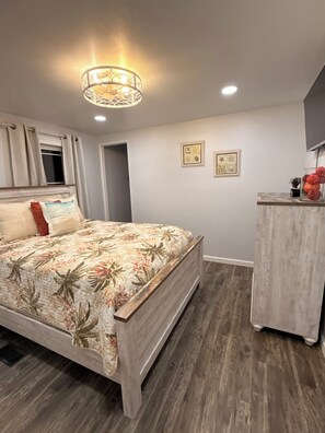 Quarto com cama, mesa de cabeceira, televisão na parede e luminária no teto.