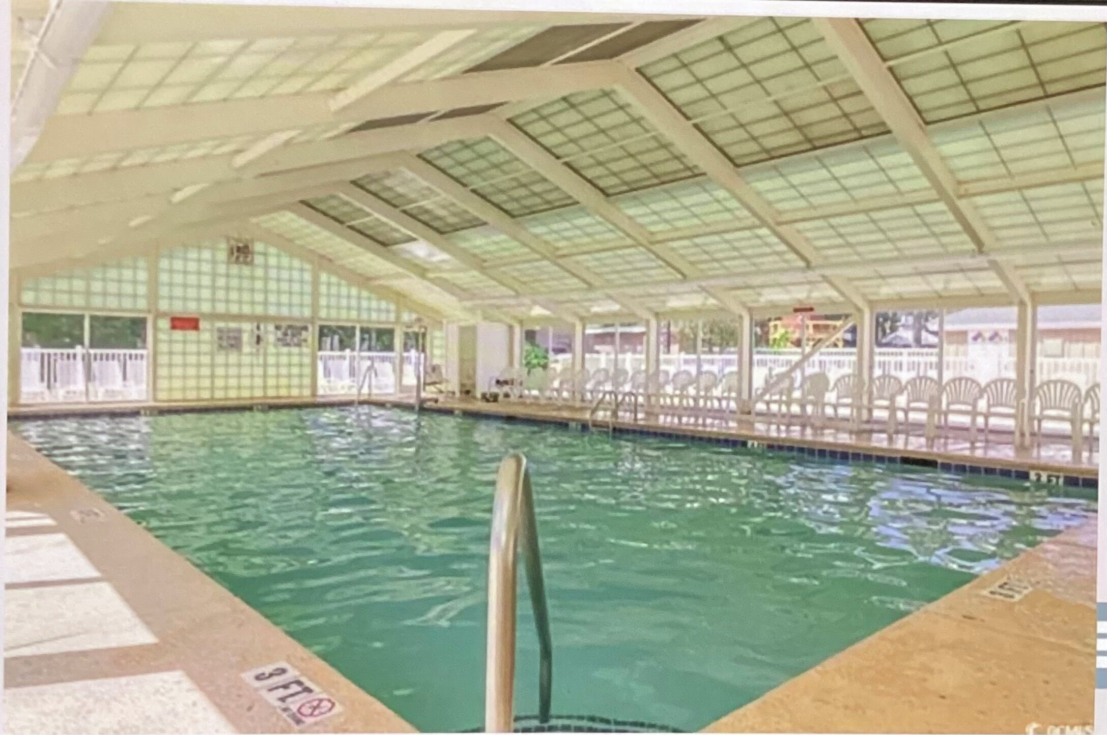 En inomhuspool med ett kaklat golv, ett glastak och en poolstege.