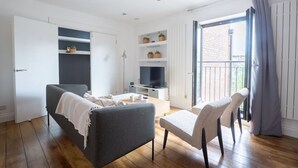 A modern living room with a grey sofa, a small table, a TV, and a balcony with a view.