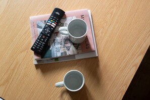 A remote control, two mugs, and a magazine on a wooden table. - King Bed, Full Kitchen | Blackout Curtains (London)