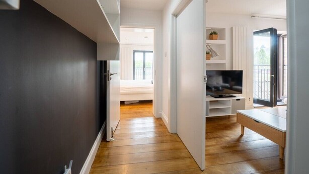 A modern apartment with a wooden floor, a TV, and a balcony.