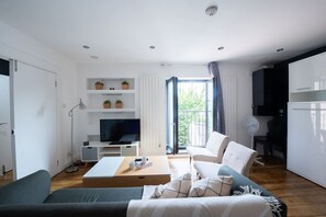 A modern living room with a sofa, coffee table, TV, and a balcony with a view. - King Bed, Full Kitchen | Blackout Curtains (London)