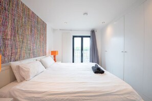 Habitación de hotel con una cama grande, un cuadro abstracto de colores, una ventana con cortinas y un armario.