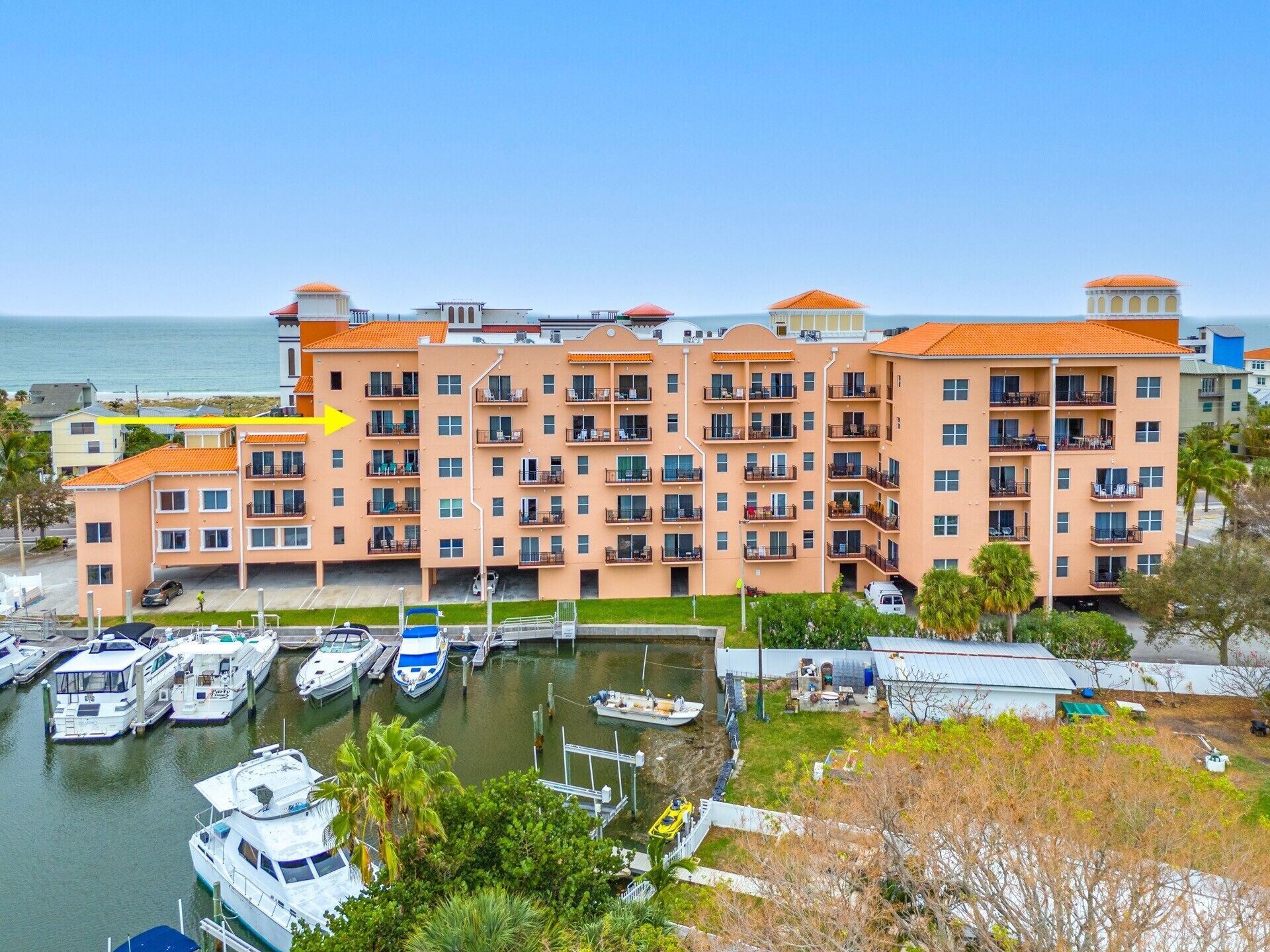 A multi-story hotel with balconies, a marina with boats, and a view of the sea.