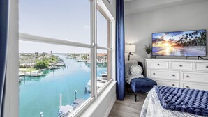 Une chambre avec une grande fenêtre donnant sur un port de plaisance, un lit, une commode et un téléviseur posé sur un meuble.