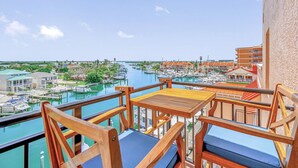 Een balkon met houten meubels met uitzicht op een jachthaven met boten en gebouwen.