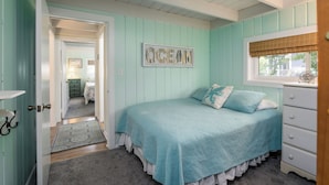 Un dormitorio con una decoración azul turquesa, una cama con colcha, un aparador y una ventana con vistas.