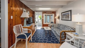 A cozy living room with a patterned sofa, a dining area with a table and chairs, and a kitchen area with wooden cabinets and a television.