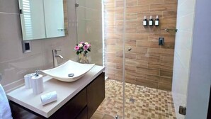 A modern bathroom with a glass shower enclosure, a large mirror, and a vanity with a sink.